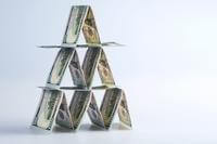 Folded 100-dollar bills form a pyramid that looks like a house of cards.