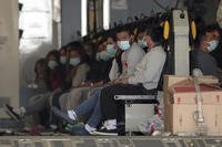 Migrants wearing face masks and shackles on their hands and feet sit on a military aircraft at Fort Bliss