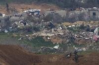 A Palestinian man wearing a red shirt, left, stands amidst the rubble of destroyed buildings