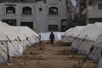 A man walks between tents for displaced Palestinians next to destroyed buildings