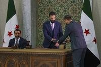 Syria's interim president Ahmad Al-Sharaa, center, prepares to sign a temporary constitution for the country in Damascus, Syria.