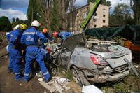 Emergency workers inspect a damaged car close to the multi-storey residential house that was ruined by a Russian missile
