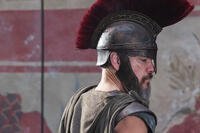 Side profile of Matt Damon wearing a bronze plumed helmet and dark armor as Odysseus in Christopher Nolan’s The Odyssey.