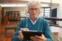 Gentleman in a library listening to an audiobook on a tablet with headphones. Photo credit: Kampus Production, image made available under creative commons and fair use.