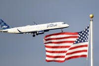 FILE - In this Sept. 21, 2018, file photo, a plane flies past the American flag in Washington. JetBlue Airways Corp. reports earnings Tuesday, July 23, 2019. (AP Photo/Susan Walsh, File)