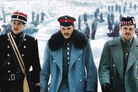 Three World War I officers in winter uniforms walk through a snowy landscape while groups of soldiers gather in the background.