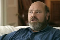 Rob Reiner sitting on a white couch during a 1990s television interview, wearing a blue shirt and speaking thoughtfully.