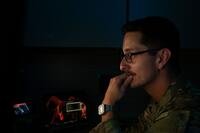 An airman in a darkened room looks at a computer.
