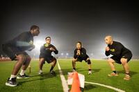 Four U.S. soldiers wearing Army PT gear do squats on a soccer field at night.