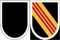 The Army's 5th Special Forces Group's existing beret flash (left) is a black shield-shaped embroidered item with a semicircular base. The new flash (right) reverts back to include alternating yellow and scarlet stripes. (Army Institute of Heraldry)