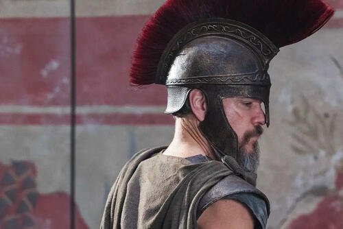Side profile of Matt Damon wearing a bronze plumed helmet and dark armor as Odysseus in Christopher Nolan’s The Odyssey.