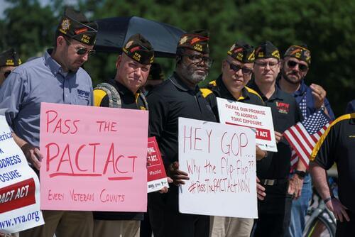 Veterans hold signs supporting the PACT Act.