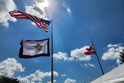 Three flags against the sky, one with a gold star.